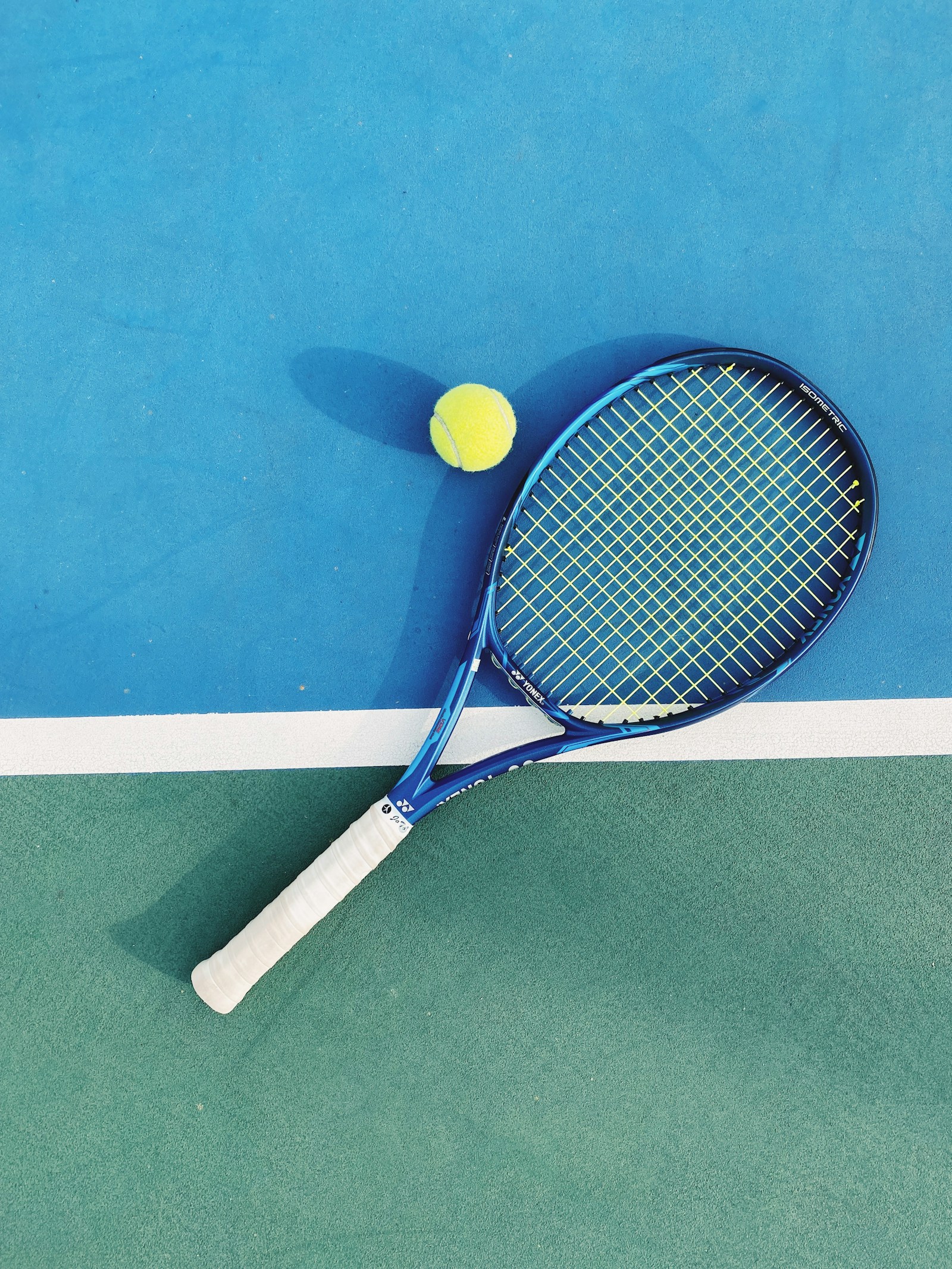 Blue tennis racket and yellow ball on a sunlit court